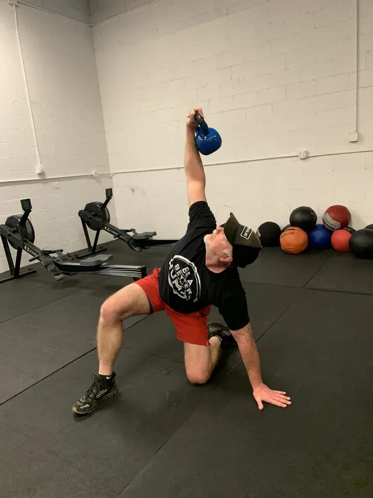 A member holding a kettlebell overhead during a Turkish get-up