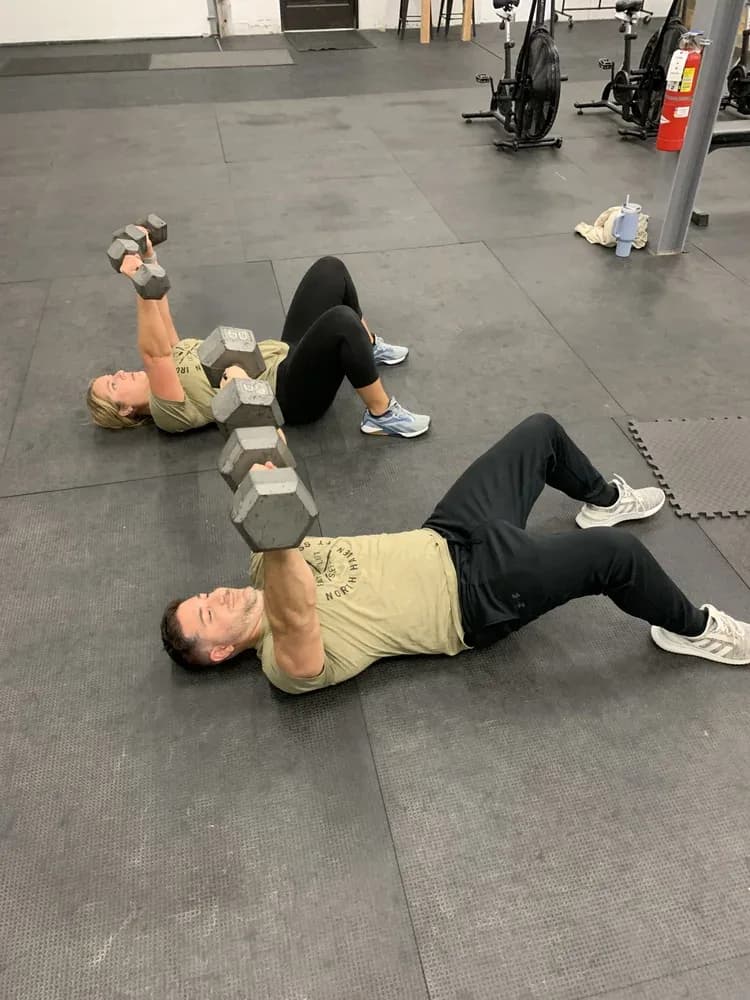 Two members doing dumbbell floor presses side by side